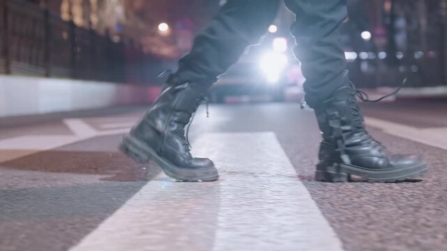 Night city crosswalk combat boots stride, lone pedestrian moves across zebra under harsh headlights, wet asphalt reflecting neon, heavy laced boots scuffing paint, cinematic tension and urban