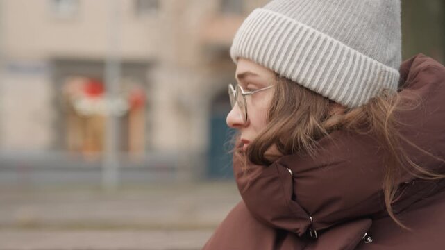 Caucasian woman writer thoughtful winter park, eyes closed against cold, layered coat and knit hat, glasses catching soft light, introspective pause on bench, cinematic calm and cozy mood