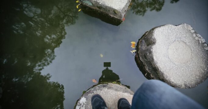 Point of view of man walking on stone steps across Japanese pond during spring