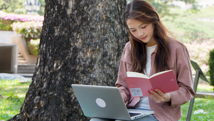 Fototapeta premium Asian University Student Studying with Laptop and Book in Sunny Campus Park