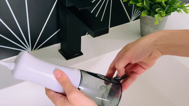 Water oral flosser held near faucet with modern design and clear reservoir for easy viewing of water level
