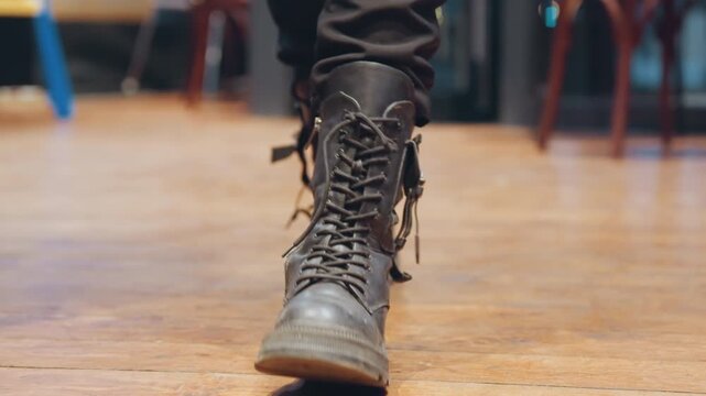 Closeup boots briskly walking across floor, combat boots with loose laces, energetic stride, heel lift, cafe interior, motion blur, upbeat rhythm, urban dancer vibe, handheld tracking, evening lights,