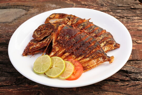 Spicy king fish fry served with lemon slices in a white plate on a wooden background.