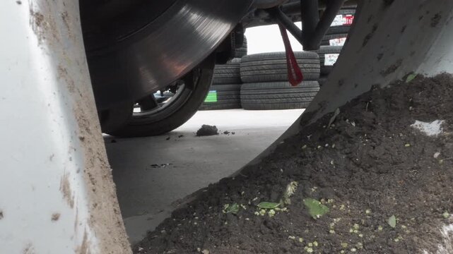 Closeup wheel arch mud accumulation pressing against rotor and fender, soil and plant fragments trapped in cavity, damp concrete undercarriage, stacked tires and red jerrycan visible in background,