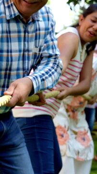 Indian Asian multigenerational family of six camping outdoors, enjoying a fun game of tug of war or Rassi Khech together, creating joyful moments in nature