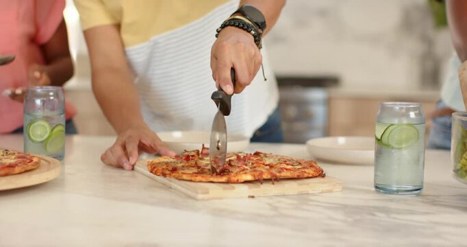 African American couple slicing pizza at counter, man in yellow tee grabbing cutter serving slices
