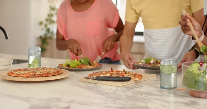 African American family seeing pizzas on marble counter, preparing salad at kitchen island for meal