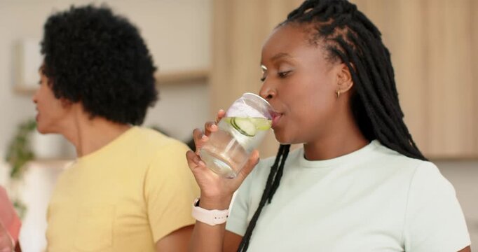 Friends in kitchen, yellow shirt speaking, right woman sipping cucumber water glass, copy space
