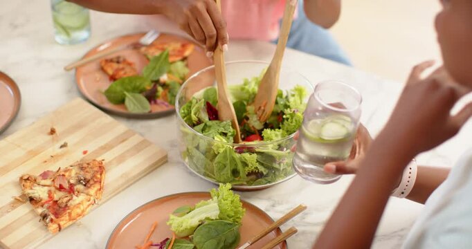Wooden servers are starting to toss salad in clear glass bowl on marble tabletop, serving plates