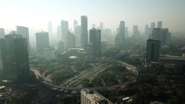 Aerial drone video of Jakarta city skyline during hazy morning featuring Semanggi cloverleaf interchange and highway traffic.
