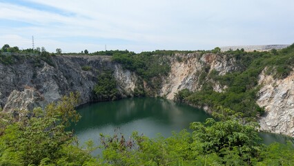 Obraz premium An old canyon where crushed stone production has ceased. The canyon is overgrown with plants, and a deep green lake has formed at the bottom.