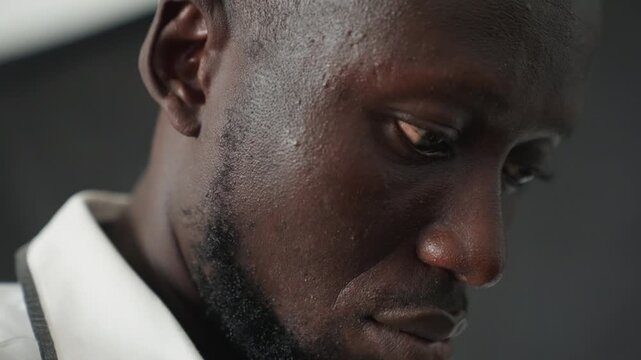 Close up sweaty man looking down, pensive portrait in lowlight studio, shallow depth of field, visible beard and collar, subtle grain, quiet mood, introspective expression, soft shadows, emotional