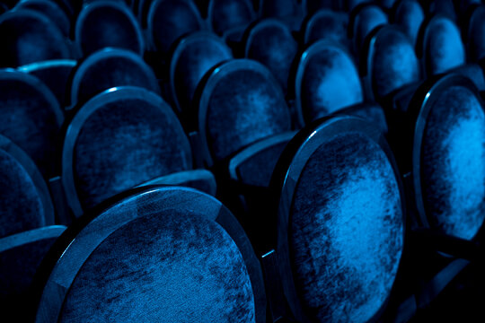 Rows of empty velvet seats in dark blue concert hall or theater