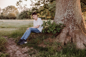 Obraz premium Teenage boy sitting beside large tree in peaceful meadow portrait