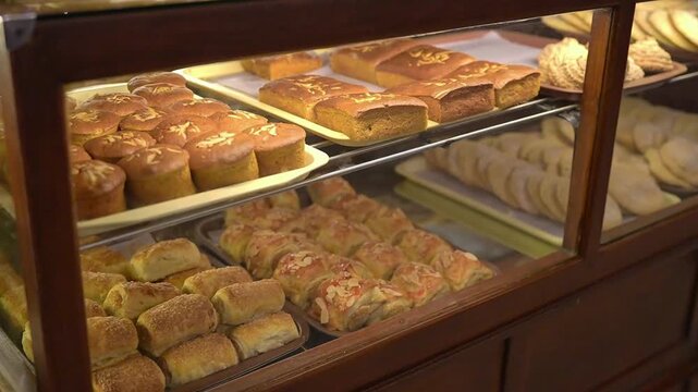 Fresh bakery pastries and cakes displayed in a glass case, warm artisan bread showcase for cafe and commercial food content.