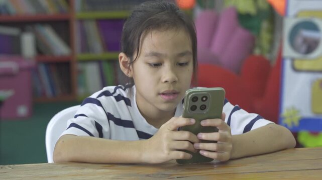 Little Asian girl using a smartphone for mobile learning and educational apps at her desk.