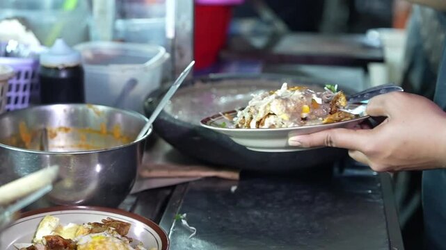 Street food vendor pouring sauce over a plated Indonesian dish, close-up local food preparation scene for authentic culinary footage.