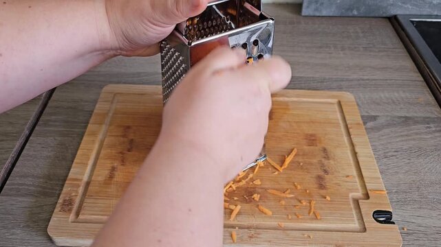 Person's hands grating carrot on a metal grater