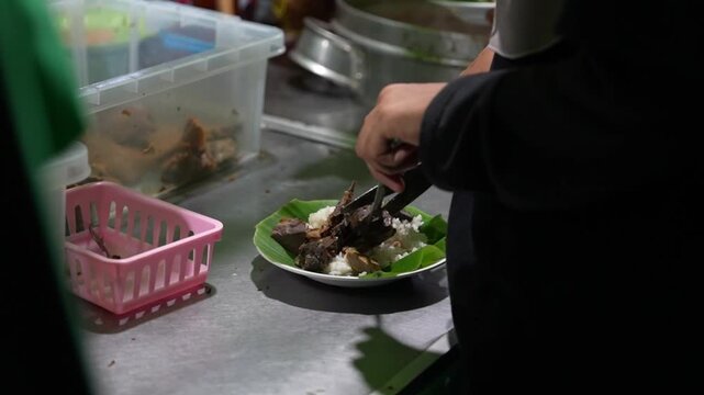 Street food vendor plating a rice meal on a banana leaf-lined plate in a kitchen, authentic Indonesian food preparation footage.