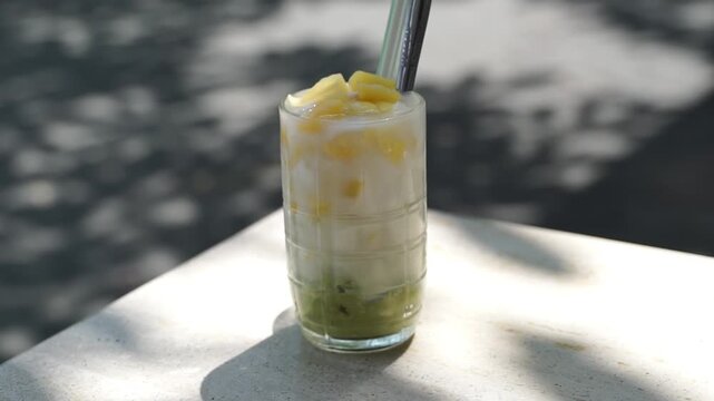 Refreshing iced avocado dessert drink with coconut milk and jackfruit topping, tropical Indonesian beverage in bright sunlight.