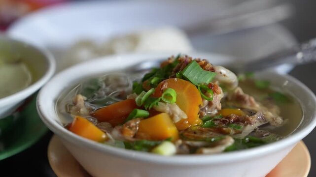 Steaming Indonesian chicken soup with vegetables, clear broth, and herbs in a cinematic close-up food shot.