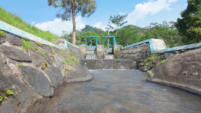 A serene water channel flowing through a rocky path under a clear blue sky with vibrant green vegetation harmonizing with nature
