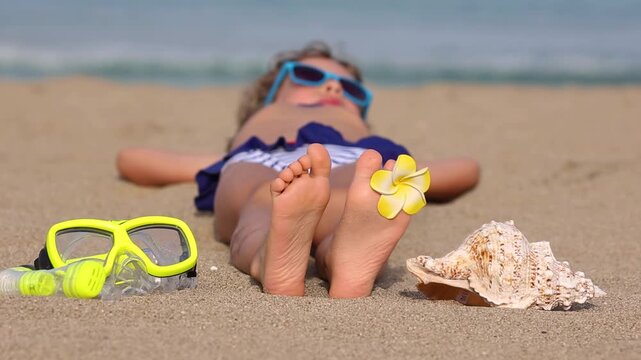 Funny kid is sunbathing on the beach during the summer vacation. Slow motion