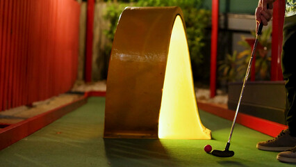 Fototapeta premium Mini Golf Player Aiming Ball Toward Glowing Yellow Tunnel Obstacle