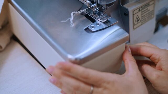Woman's hands opening an industrial overlocker sewing machine to reveal its internal mechanism