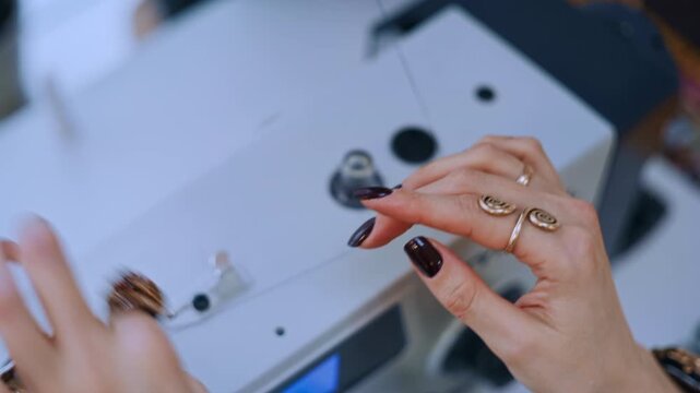 Woman's hands placing a spool of thread on a sewing machine, preparing for needlework