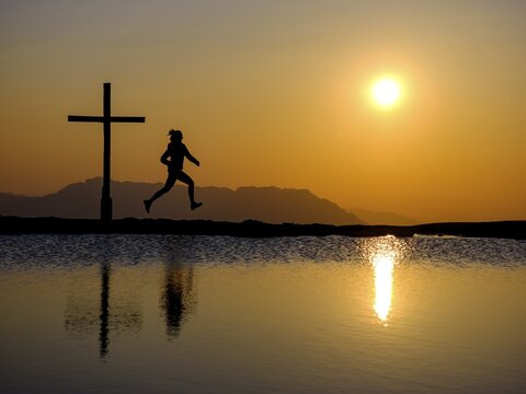 Silhouette of a runner with summit cross at sunset, reflection in the water, Trattberg, Bad Vigaun, Land Salzburg, Austria