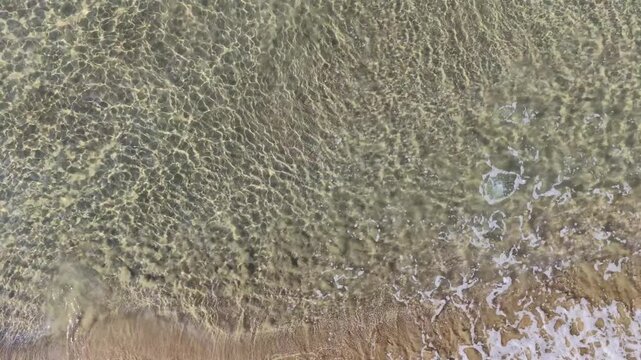 Il bagnasciuga della spiaggia col mare calmo e cristallino.
Vista dall'alto delle onde sulla sabbia della spiaggia. Ripresa in 4K
