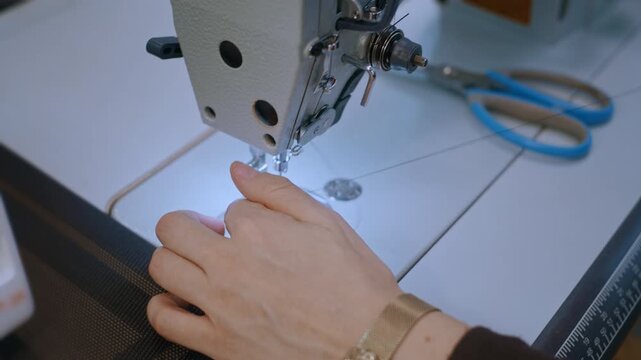 A female dressmaker operates a high-speed industrial sewing machine