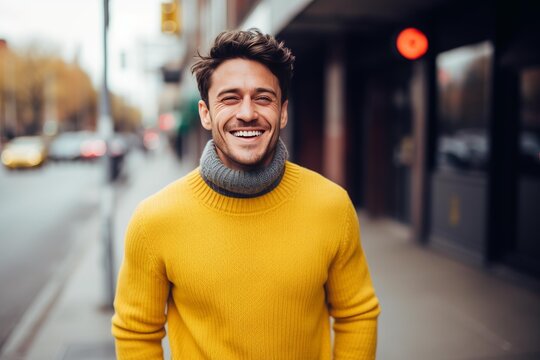 Smiling man wearing yellow sweater and turtleneck standing on an urban street