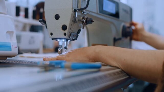 Close-up of a worker's hands sewing on an industrial machine in a textile factory workshop