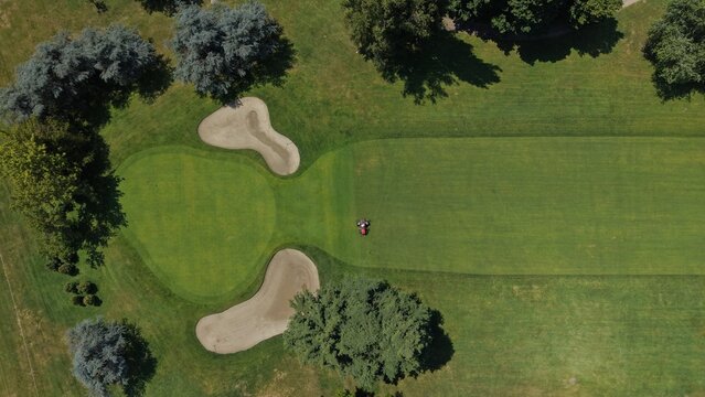 Golf Course Aerial View: An aerial perspective captures a lush green golf course with a flag on the putting green, surrounded by trees and sand bunkers.