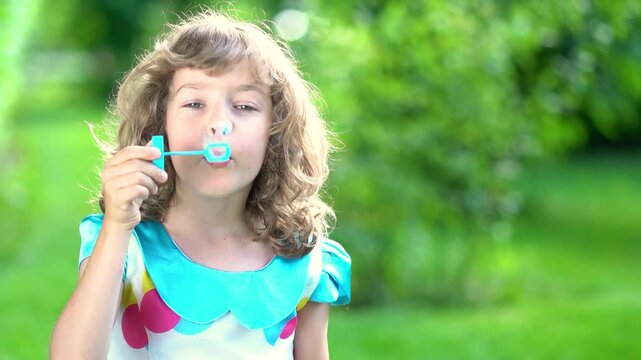 A happy child blows soap bubbles in a summer park. Slow motion