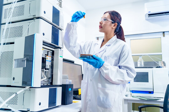 Scientist in lab coat and gloves examines liquid sample near advanced chromatography equipment