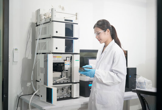 Scientist in lab coat and gloves examines samples near advanced chromatography equipment