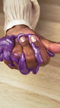 Metallic purple slime squeezed in hand, shimmering gooey texture being pulled through fingers, satisfying ASMR sensory play with viscous glitter putty