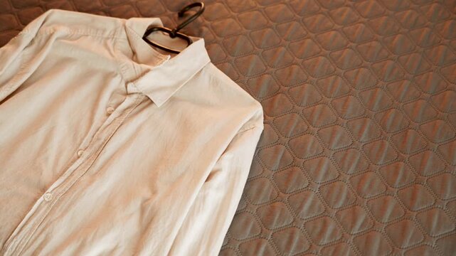 Preparing a beige long sleeve shirt with hanger on textured bed
