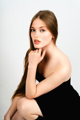 Fototapeta premium Close-up portrait of a woman crouching with her hand supporting her chin against a solid white studio background.