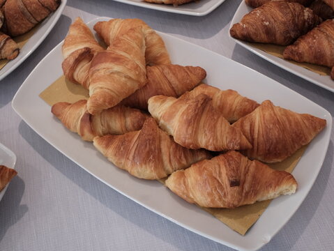 Vista dall'alto di un vassoio di cornetti artigianali sfogliati e dorati, perfetti per la colazione al bar o una pausa dolce.