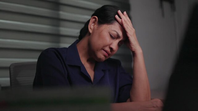 Overwhelmed Professional: A businesswoman sits at a desk, head in hands, overwhelmed and distressed by work pressure and deadlines, conveying a sense of mental exhaustion and anxiety.
