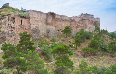 Fototapeta premium Stone walls of Narikala Fortress on a green hill in Tbilisi