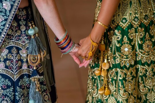 Close-up of two women holding hands in traditional Indian bridal lehenga dresses at a wedding ceremony