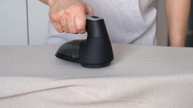Hand removes pills from knitted clothing using fabric shaver. Textile pilling. Linting. Fabric lint, pilly, pellet, fluff
