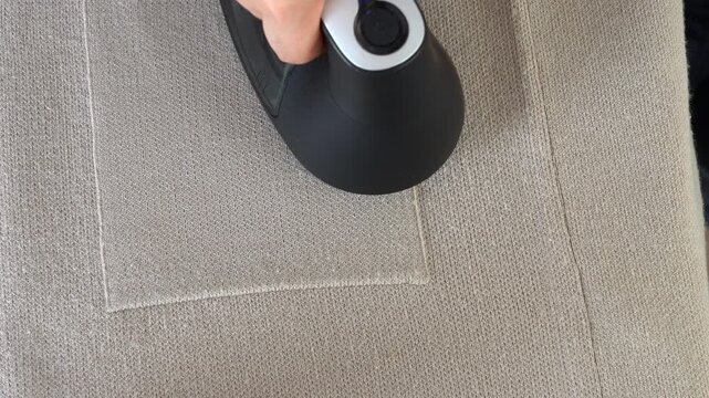 Top view hand removes pills from knitted clothing using fabric shaver. Textile pilling. Linting. Fabric lint, pilly, pellet, fluff