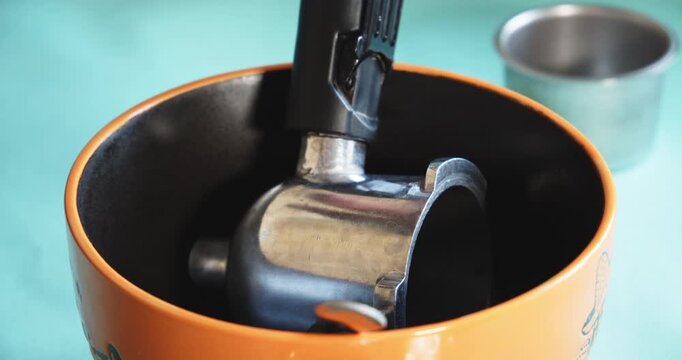 Close-up of a metal coffee machine portafilter soaked in a deep orange bowl to remove coffee sediment