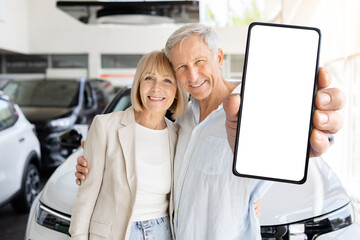 Obraz premium Senior man showing smartphone with blank screen beside partner at car dealership showroom, ideal for automotive app promotion and digital advertising use